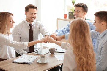 Young people in office wear putting hands together indoors. Unity concept