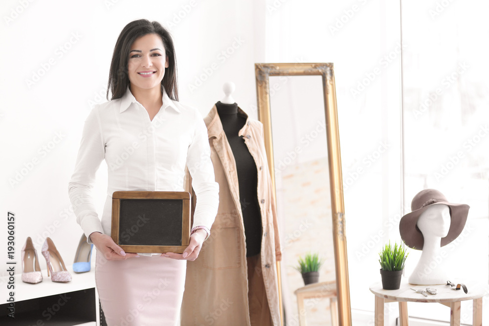 Wall mural Portrait of young woman with mini chalkboard in boutique. Small business owner