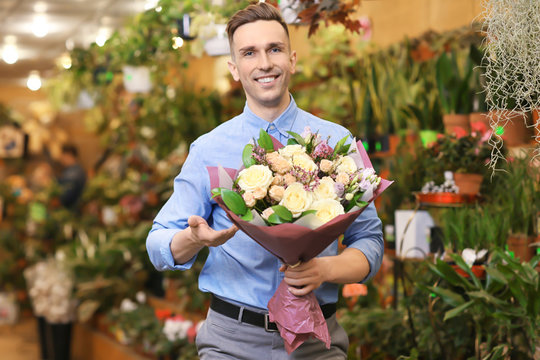 Portrait of young man with flowers in greenhouse. Small business owner