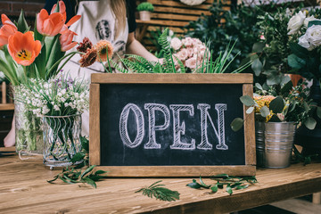 Wooden table with floral arrangements and blackboard saying Open in flower shop. 