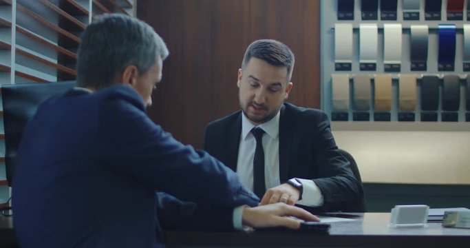 Elegant man paying with credit card then receiving car key in showroom