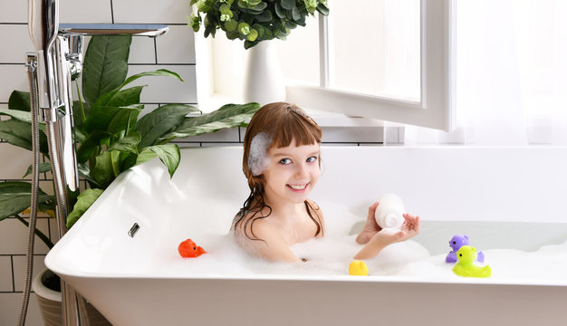 Happy little baby girl sitting in bath tub play with yellow duck toy in the bathroom