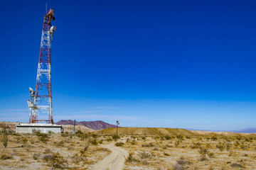 Large Red and White Microwave Tower in the Middle of the Anza Borrego Desert with Bright Blue Sky and Mountains in the Background