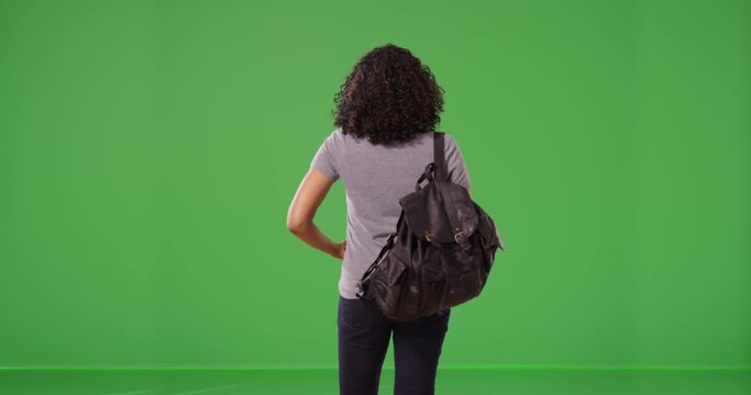 Rear view of black woman with backpack taking photo using smartphone greenscreen. Tourist taking picture with mobile phone on green screen to be composited or keyed. 4k
