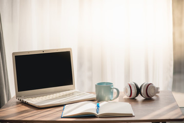 Coffee mug with notebook white laptop and headphone on table near window, work lifestyle concept.