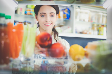 Portrait of female standing near open fridge full of healthy food, vegetables and fruits. Portrait of female
