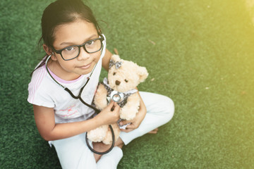 young little asian girl playing pretend to be a doctor. young girl eaxamine her teddy bear with...