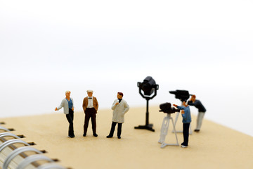 Miniature people: female journalist making an interview a man with a cameraman video camera.