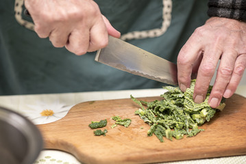 Elderly man, a domestic cook, cutting small pieces of green vegetable, borecole, to prepare for lunch
