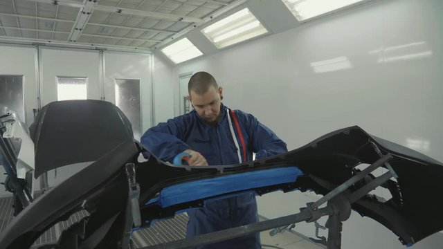 Serviceman preparing a car bodykit for painting in a workshop