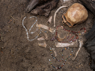 Still life of archaeological excavation with skull, bones and ancient glass beads necklace still half buried in the ground of ancient grave