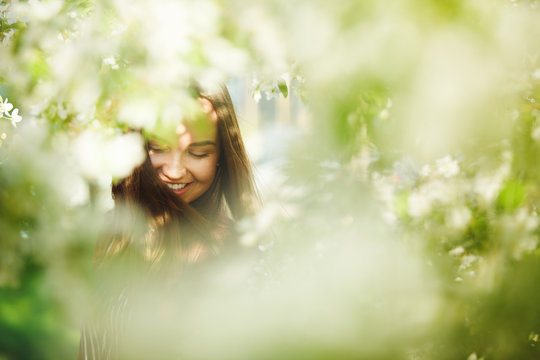 portrait of smiling and happy woman near foliage of trees.
