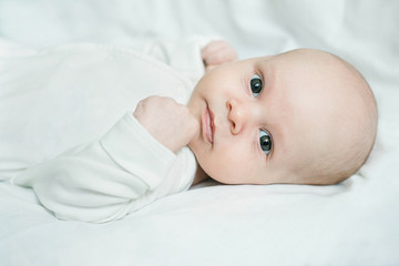 Close up portrait of three-month-old baby boy lying on white linen
