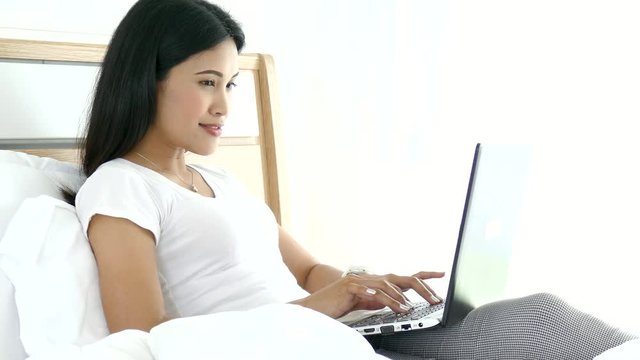 Beautiful asian woman on bed is using her laptop to browse the web. 
