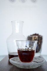 Coffee in a transparent cup on a wooden plank. In the background is a jar of coffee aroma and coffee beans. Close-up with copy space