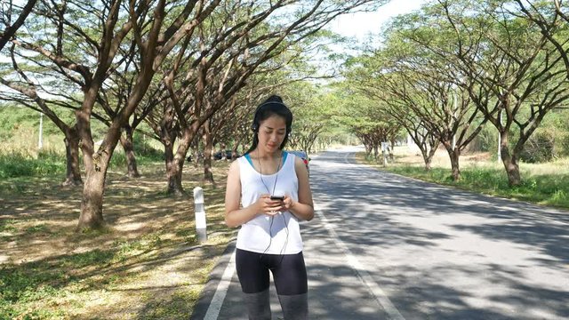 4k of Young woman listening to music with earphones on smart phone app in the park