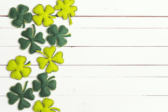 St.Patrick's day background with felt four-leaf clover on white wooden table. Space for text, top view.