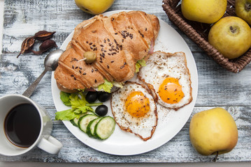Breakfast. Fried Eggs with Sandwich Croissant, Cucumbers, Black Olives and Apples. Rustic Gray Background. Top view. Morning Food.