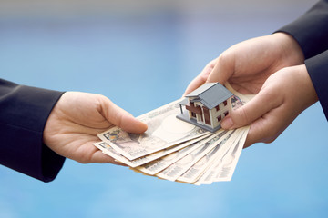 Two businessmen conduct a house sale with a model house and Yen banknotes valued at 10000 yen.using as background business concept and real estate concept with copy space for your text or design.