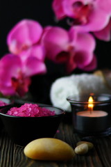 Composition of spa treatment on dark wooden background. Pink massage sea salt and orchids. Copy space