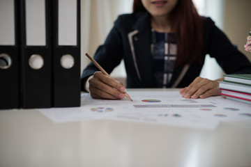 Business woman holding a pencil is working with graph on the desk related to business functions.