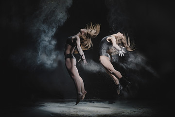 Two girls dance with flour on black background