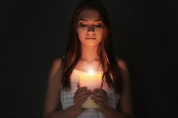 Beautiful young woman with burning candle in darkness - Powered by Adobe