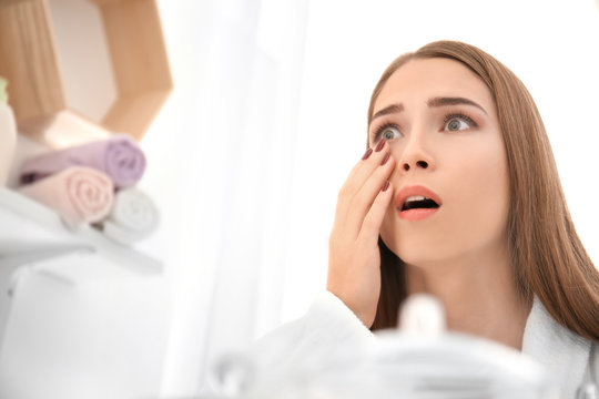 Young woman with eyelash loss problem looking at herself in mirror indoors