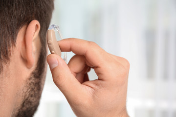 Young man putting hearing aid in ear indoors