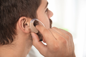 Young man putting hearing aid in ear indoors