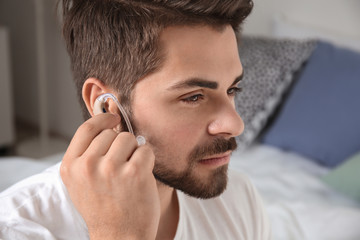 Young man putting hearing aid in ear indoors