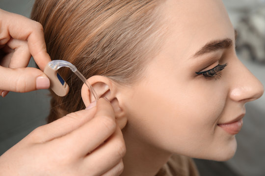 Doctor putting hearing aid in woman's ear indoors