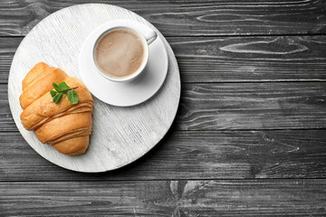 Delicious croissant with cup of coffee on wooden board