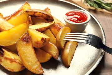 Plate with delicious baked potato wedges and sauce on table