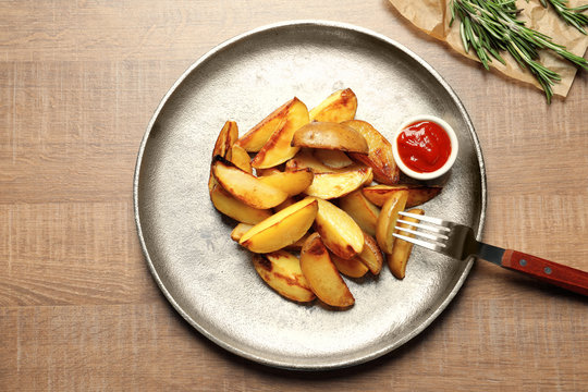 Plate with delicious baked potato wedges and sauce on table