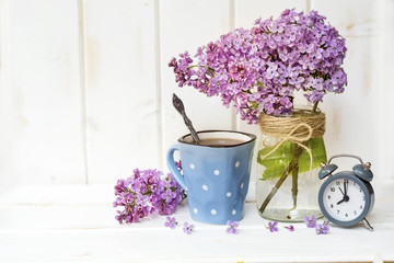 Fototapeta na wymiar Bouquet of Lilac with Alarm Clock and Cup of Coffee on white Wooden Background .Morning Concept