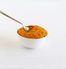 Turmeric powder, or haldi, traditional and popular ingredient used in many Indian dishes, scooped with a steel spoon from a white ceramic bowl.