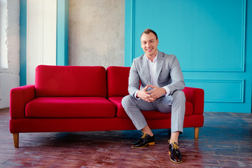 Handsome and elegant young man sitting on the red couch.
