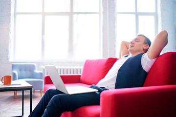 Working and relaxing at home. Young man using laptop computer while sitting on sofa.