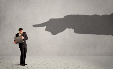 Business person looking at huge shadow hand pointing at him concept