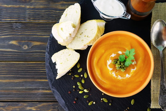 Pumpkin and carrot soup with cream and parsley on dark wooden background. Top view.  Copy space