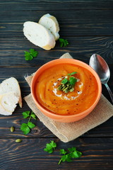 Pumpkin and carrot soup with cream and parsley on dark wooden background. Top view.  Copy space