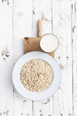 Oatmeal, rolled oats on white wooden background wilt glass of milk. Porridge oats, used in granola or muesli. Breakfast concept