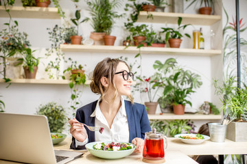 Businesswoman working during the lunch with salad sitting at the vegan restaurant on the beautiful green wall background