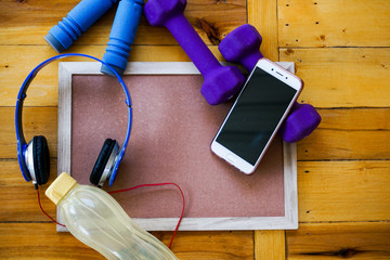 Sports, fitness concept. Running sneakers, water bottle, headphones, dumbbells, smartphone, on wooden background top view copy space