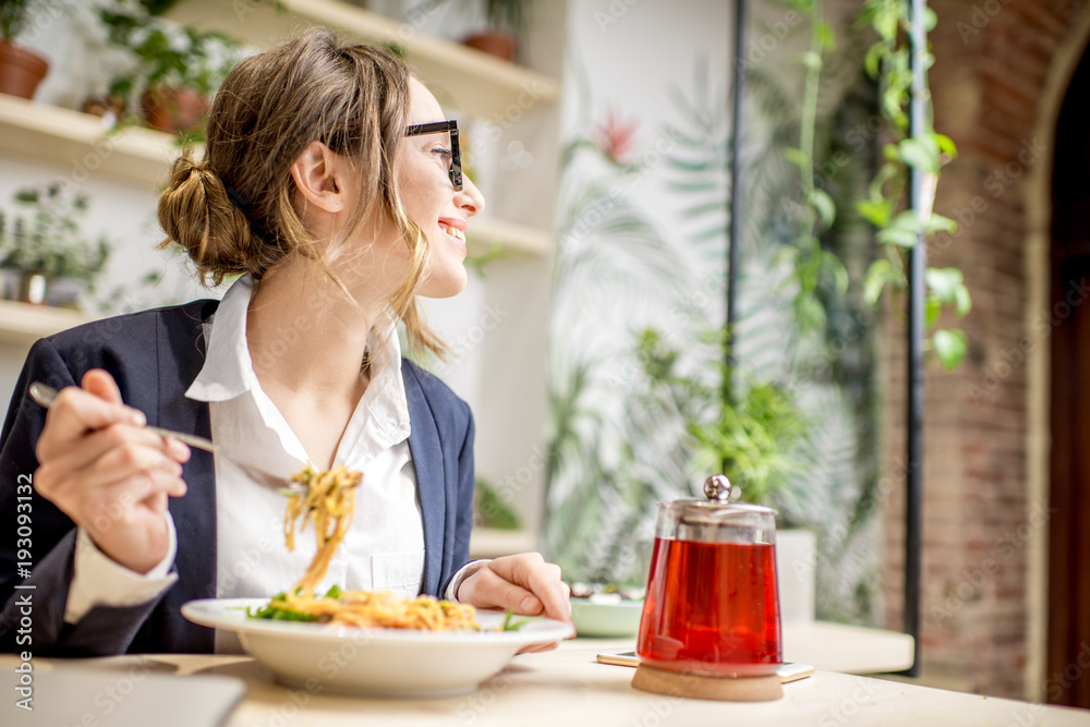 Wall mural Businesswoman having lunch with pasta and fruit tea at the vegan restaurant on the green background