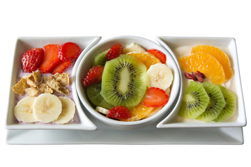 Fresh fruit salad served along with strawberry greek yogurt topped with strawberries, cereal and bananas, and orange greek yogurt topped with oranges, goji berries and kiwis