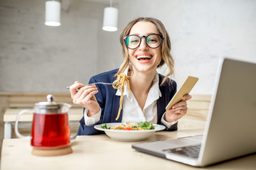 Businesswoman enjoying pasta meal sitting with laptop at the white cafe interior