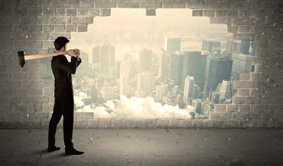 Business man hitting wall with hammer on city view