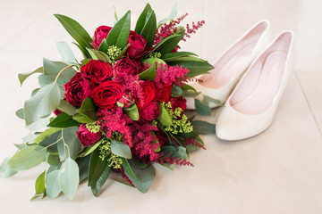 Delicate, expensive, trendy bridal wedding bouquet of flowers in marsala and red color. Wedding bouquet with red roses and greenery in focus beige shoes on background. Wedding accessories. 